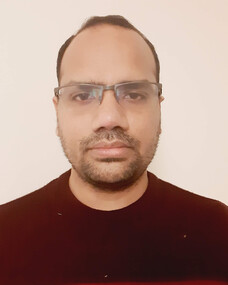 Himanshu mit Brille und dunklem Pullover, ernster Blick.